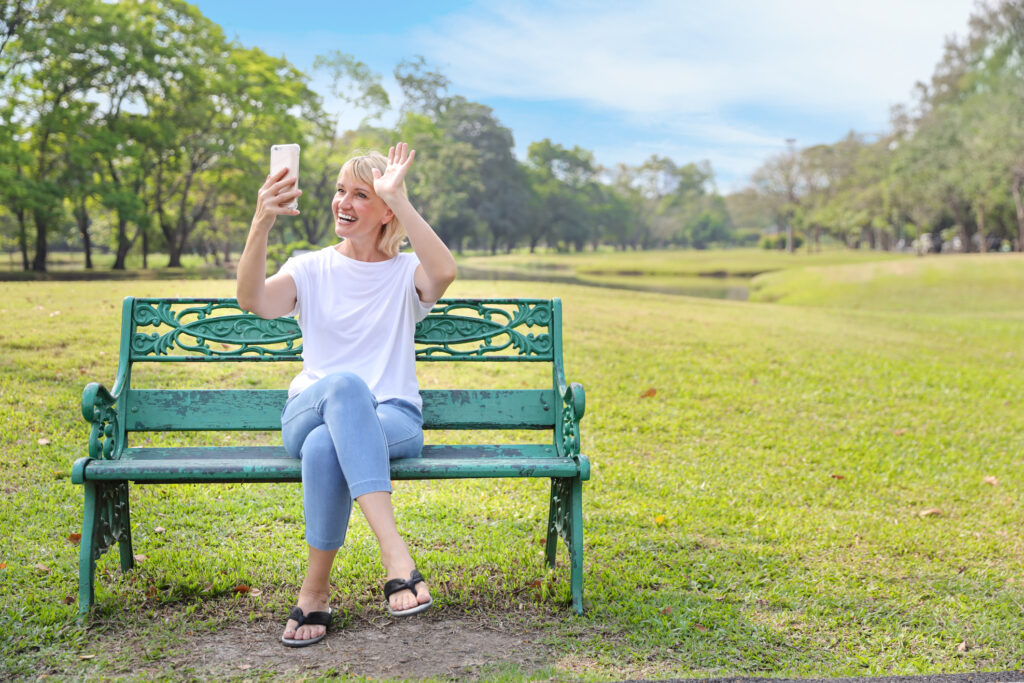 Frau mittleren Alters sitzt im Park und macht einen Viedeo call